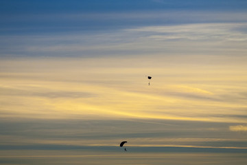 Silhouette of two skydivers falling with parachute open against dramatice sunset and clouds