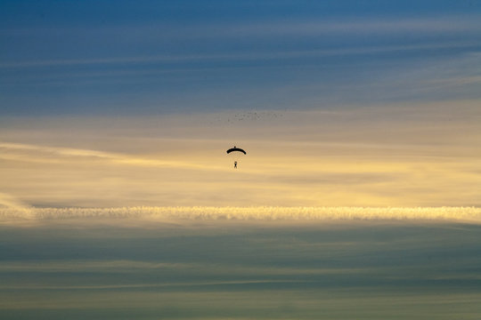 Silhouette of lone skydiver falls with parachute open against dramatice sunset and clouds