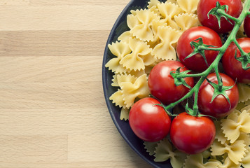 Red tomatoes on pasta on plate on wood