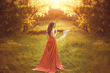 .Beautiful young princess in a long red dress walks among the green plants in the woods , a fashionable toning , creative color