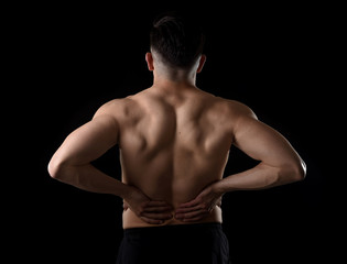 Fototapeta premium young muscular body sport man holding sore low back waist with his hands suffering pain in athlete stress and health care concept isolated on black background