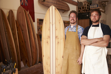 Portrait of smiling carpenters standing with surfboard in workshop