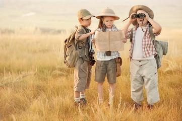 Group of kids travelers read a map at sunset - obrazy, fototapety, plakaty