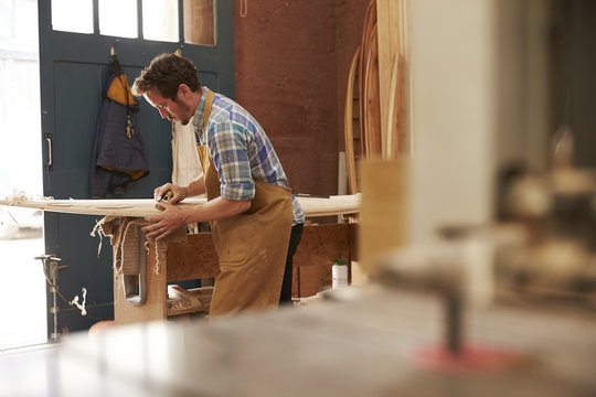 Carpenter Planing Bespoke Wooden Surfboard In Workshop