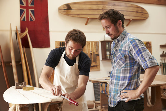 Carpenter With Apprentice Making Bespoke Wooden Surfboard
