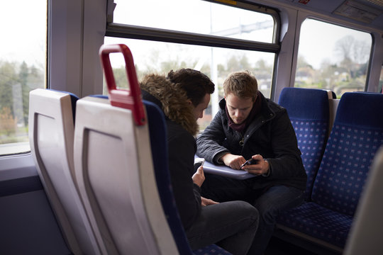Two Men Sitting In Train Carriage Looking At Text Message