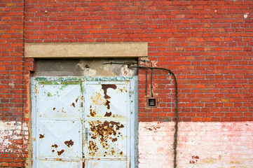 Old abandoned industrial building - detail of white rusty doors and facade made of red bricks