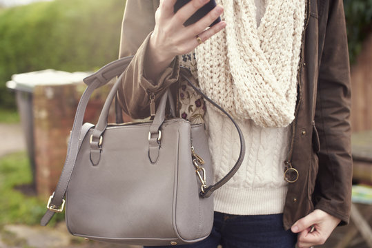 Woman Walking Outdoors Holding Handbag And Mobile Phone