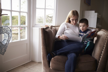 Mother reading story to her son while sitting on armchair at home