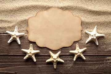 Fototapeta na wymiar Blank paper label and starfishes on sand and wooden table