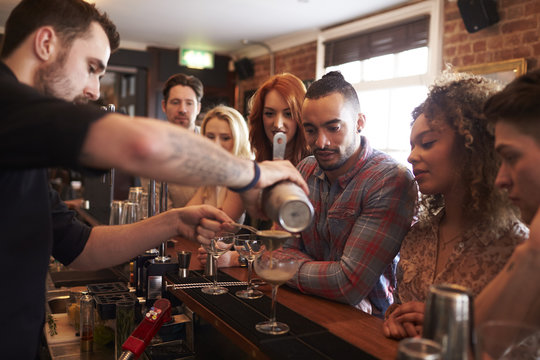 Bartender Giving Cocktail Making Lesson to Friends In Bar