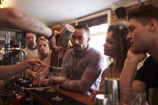 Bartender Giving Cocktail Making Lesson to Friends In Bar