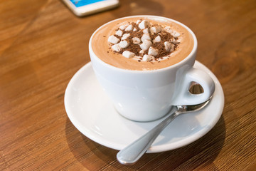 Cup of hot milk chocolate with marshmallows and smartphone on wooden table