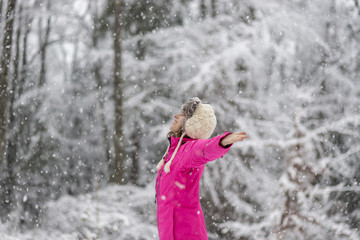 Fototapeta na wymiar Happy young woman standing in snow blizzard with her arms spread