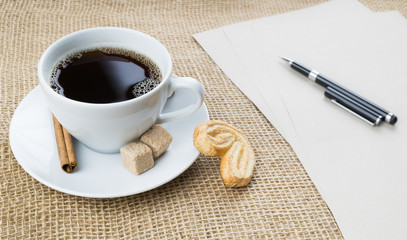 Cup of coffee, cookie, pen and paper on sackcloth background