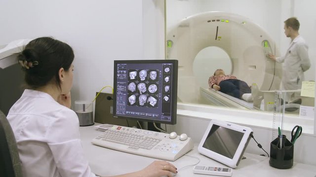 Dark-haired doctor looking at computer screen while patient moving in mri machine