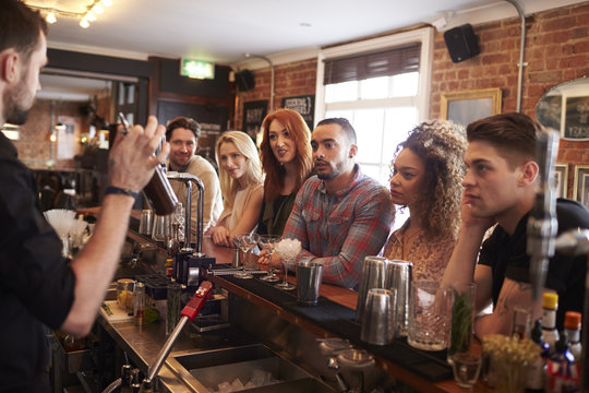 Bartender Giving Cocktail Making Lesson to Friends In Bar