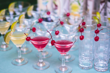 Beautiful row line of different colored alcohol cocktails with mint on a tropical Hawaiian hawaii style party, martini, vodka,and others on decorated catering bouquet table on open air beach event
