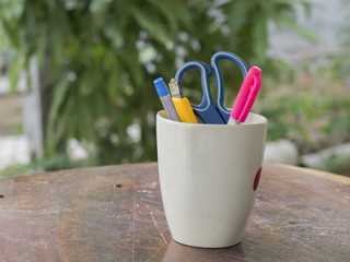 Colorful pens in white cup on wooden table