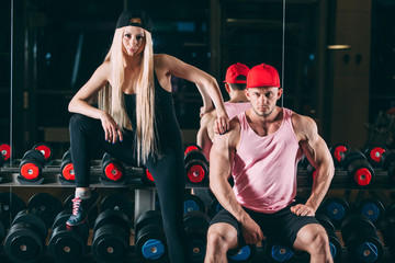 Fototapeta na wymiar sport, bodybuilding, weightlifting, lifestyle and people concept - Young beautiful couple in stylish clothes sitting a gym near the dumbbells