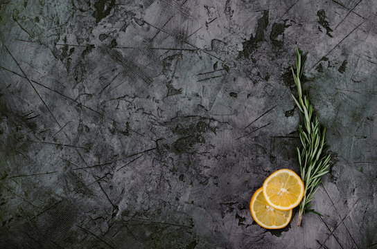 cooking background with rosemary and two sliced lemons on black stone table.