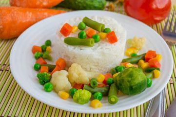 Rice with vegetables steamed on a white plate, laid out in a circle. Vegan. The top view.