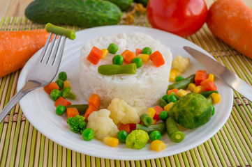 Rice with vegetables steamed on a white plate, laid out in a circle. Vegan. The top view.