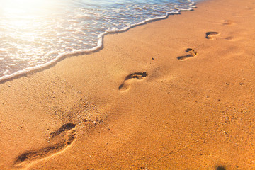 beach, wave and footprints at sunset time