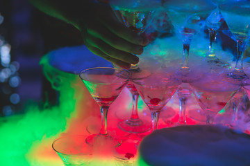 Beautiful pyramid line of multicolored different colored alcohol cocktails with mint on a tropical style party, martini, vodka,and others on decorated catering bouquet table on open air event