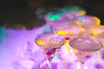 Beautiful pyramid line of multicolored different colored alcohol cocktails with mint on a tropical style party, martini, vodka,and others on decorated catering bouquet table on open air event