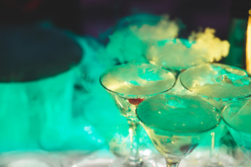 Beautiful pyramid line of multicolored different colored alcohol cocktails with mint on a tropical style party, martini, vodka,and others on decorated catering bouquet table on open air event