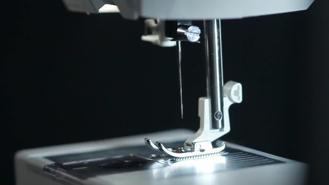 Modern sewing machine. Closeup. Manufacturing equipment at factory. Macro. Panning on steel sewing needle in slow motion. Part of modern sewing machine isolated on black background