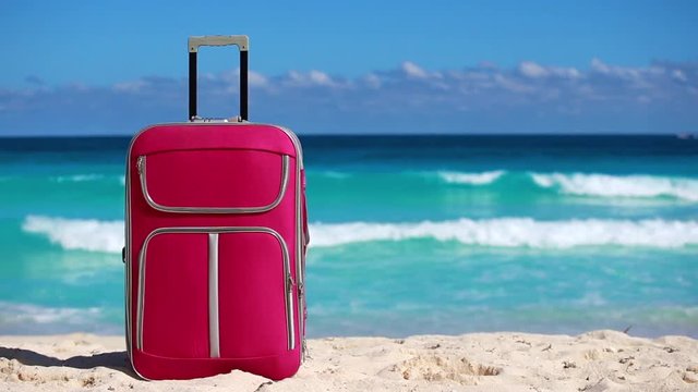 One pink suitcase on sandy tropical beach. Vacation concept
