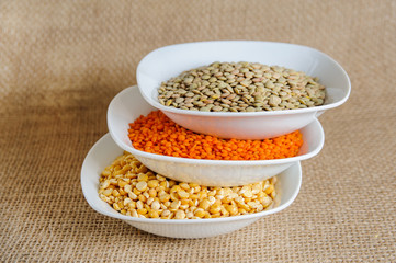 Fototapeta premium Bowls of various legumes (red turkish lentils, yellow indian lentils, green lentils) on rustic burlap background 
