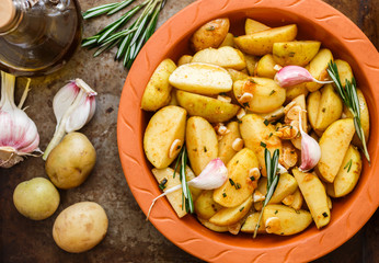 Sliced raw potatoes in a clay baking dish before baking in the oven with spices, garlic, rosemary, olive oil. Dinner in a rustic style. Selective focus
