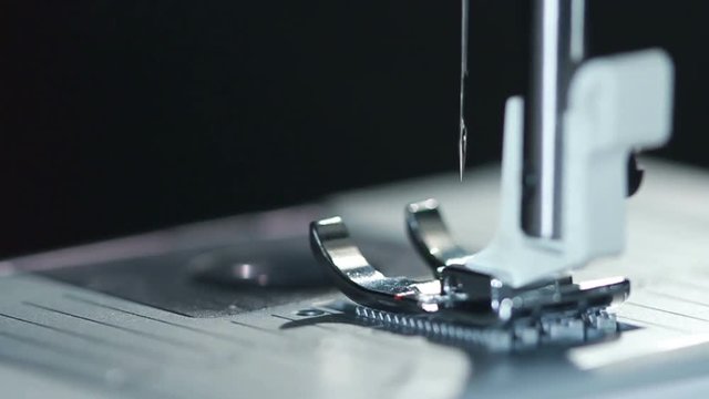 Steel sewing needle in slow motion. Modern sewing machine. Closeup. Manufacturing equipment at factory. Macro. Part of modern sewing machine isolated on black background