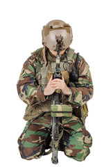 A soldier in camouflage bent over a gun. Praying and sitting with a gun. Image on white background