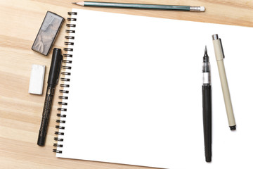Blank white notepad with pens on wooden table