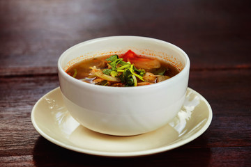 Bowl of fresh spicy hot thai soup Tom Yum at wooden table 