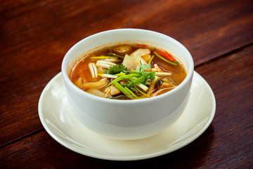 Bowl of fresh spicy hot thai soup Tom Yum at wooden table 