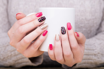 Manicure - Beauty treatment photo of nice manicured woman fingernails holding a cup. Very nice feminine nail art with nice pink, gold and black nail polish.