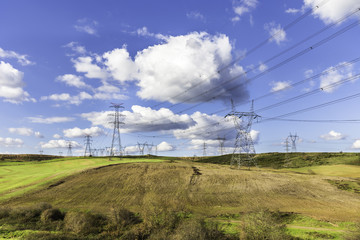 Fototapeta na wymiar Lots of high voltage power transmission towers on a natural land with blue sky background