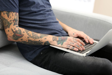Young man with tattoo using laptop on a sofa at home