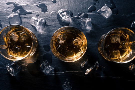 Glasses of whiskey with ice cubes on dark table