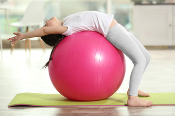 Naklejka premium Little cute girl doing exercises with ball on a mat indoor