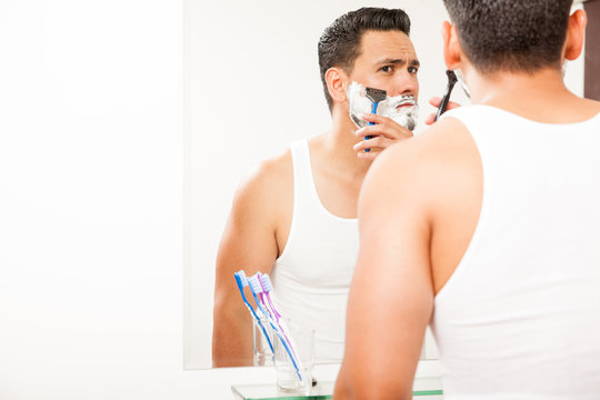 Young man shaving his beard with a razor