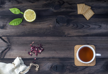 a cup of tea with tea cookies, fresh lemon and linen bag with hibiscus on wooden table