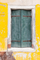 Old window with green shutters on yellow wall