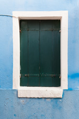 Old window with dark shutters on light blue wall