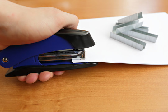 Hand holding blue stapler stapling papers, closeup view